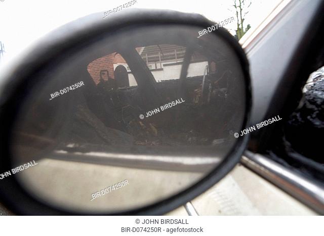 Looking at the reflection through the wing mirror of a vandalised and burnt out car in an inner city street