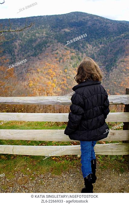 A young 9 year old caucasian girl looking over the rail at the fall leaves color changing on the North Carolina Blue ridge Parkway in the fall