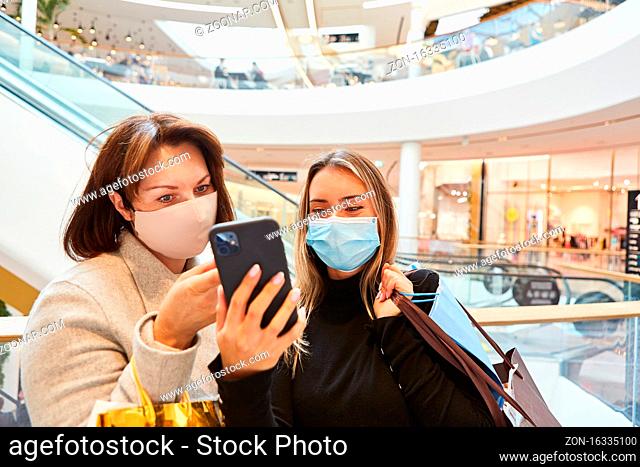 Frauen mit Mundschutz wegen Covid-19 lesen SMS auf Smartphone im Einkaufszentrum