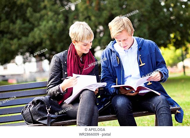Young friends studying while sitting on bench in university campus