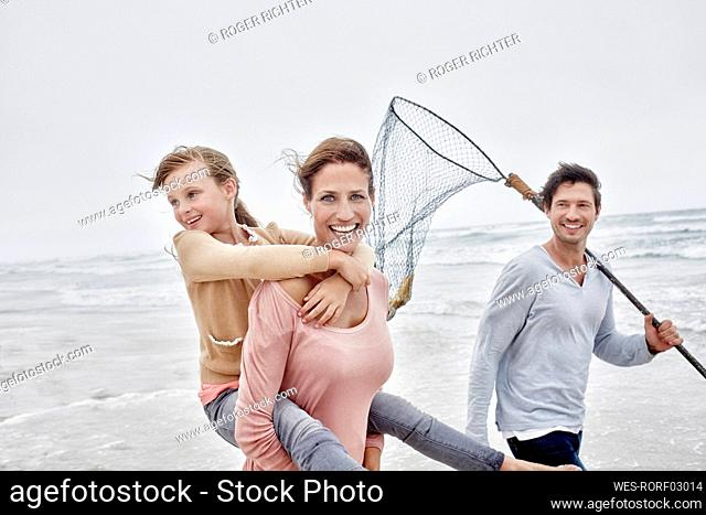 Carefree family with carrying daughter walking on the beach father holding fishing net
