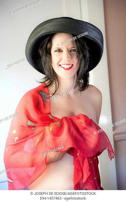 Portrait of a partially nude nineteen year old brunette woman laughing at the camera wearing a black hat