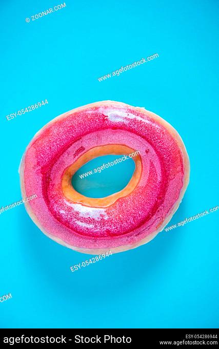 Vibrant bright pink donut on blue background, overhead