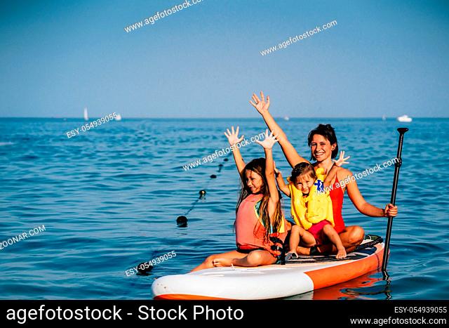 Mother with two daughters stand up on a paddle board. At sea, calm