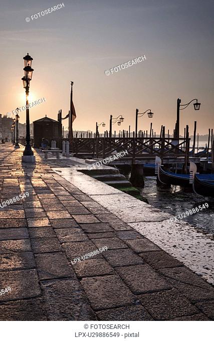 The Molo San Marco in front of Doge's Palace at dawn, with row of traditonal wrought iron lamps, view of gondola station and San Marco basin beyond, Venice