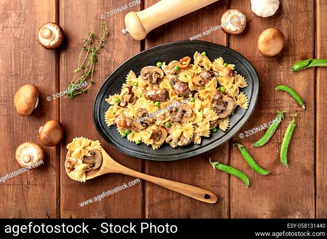 Mushroom and cheese pasta. Farfalle with cremini and green peas, shot from the top with ingredients on a dark rustic wooden background