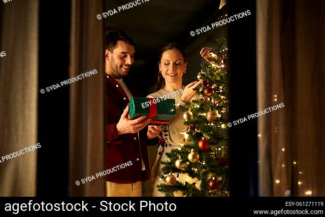 couple with gift decorating christmas tree at home
