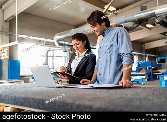 Young businesswoman working with colleague while standing in industry