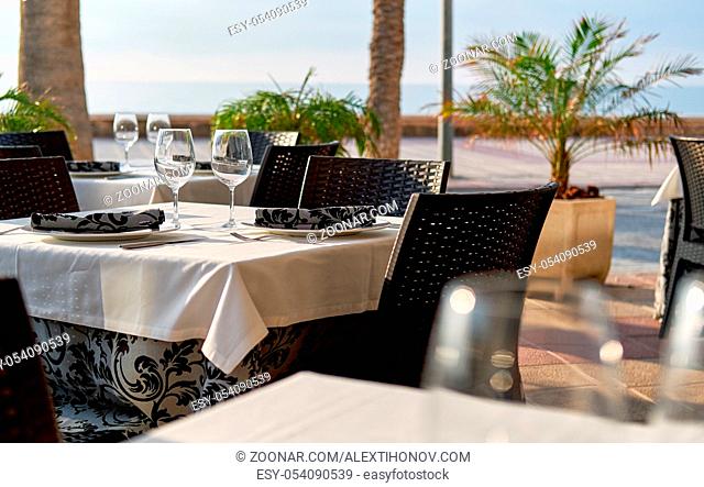Empty outdoors restaurant. Table setting with a wine glasses, cutlery and plates
