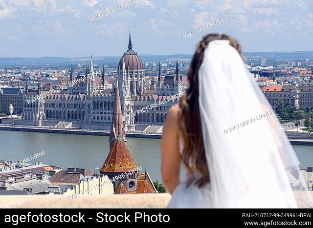 26 June 2021, Hungary, Budapest: A woman with a bridal veil stands on the Fishermen's Bastion looking at the seat of the Hungarian Parliament in Budapest