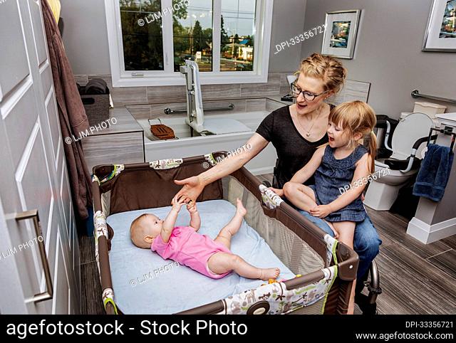 A paraplegic mother playing with her baby in a play pen and holding her daughter on her lap while sitting in a wheelchair; Edmonton, Alberta, Canada