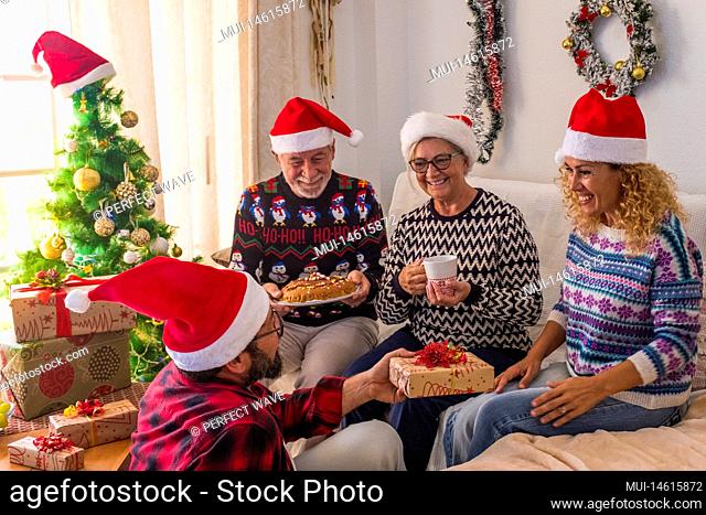 group of four mature and young people having fun at home the christmas day wrapping the presents and gifts together - man giving at his woman a gift