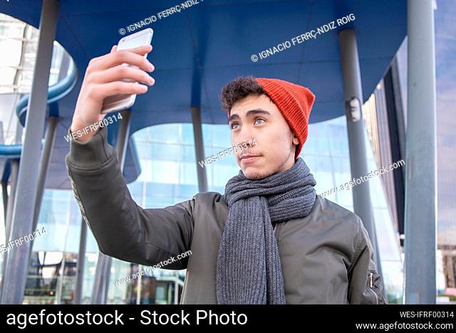 Young man wearing scarf taking selfie against modern building in city