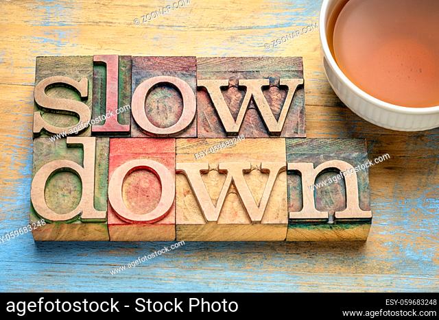 slow down - word abstract in letterpress wood type blocks with a cup of tea