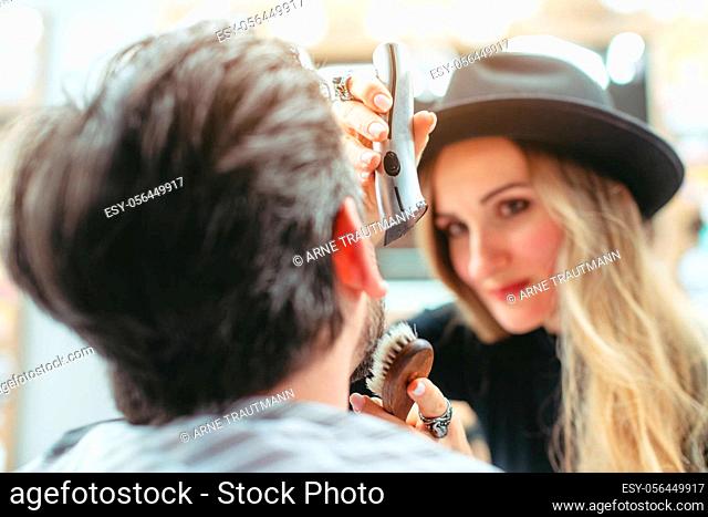 Woman barber cutting and trimming beard of client in her shop