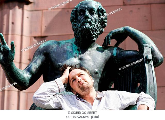 Portrait of mid adult man with hand in hair in front of sculpture, Freiburg, Baden, Germany