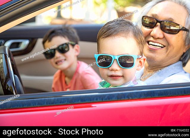 Chinese granfather and mixed-race children playing in parked car