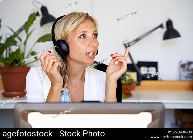 Female customer service representative gesturing while answering through headphones at office