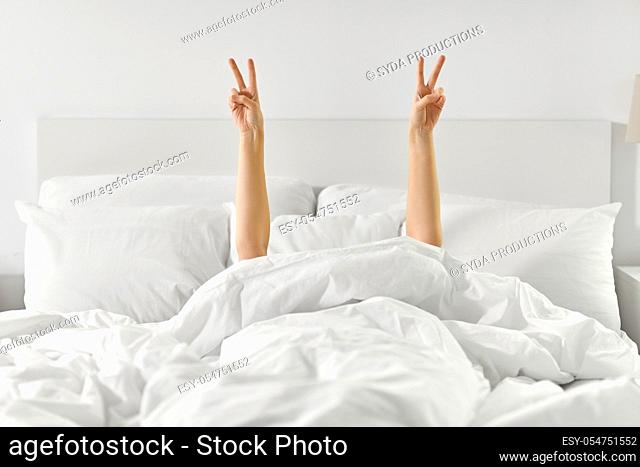 hands of woman lying in bed and showing peace