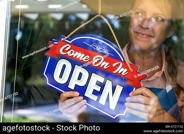 Happy Female Store Owner Turning Open Sign in Window, USA, North America
