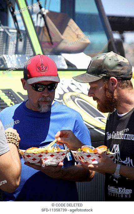 Two men eating fries at a food truck festival in California, USA