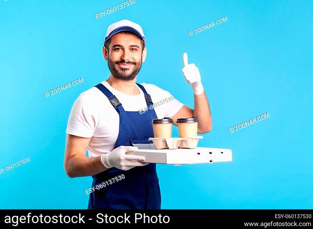 Delivery service. Friendly optimistic courier in overalls holding coffee and pizza box, wearing safety gloves offering drinks food and showing thumbs up