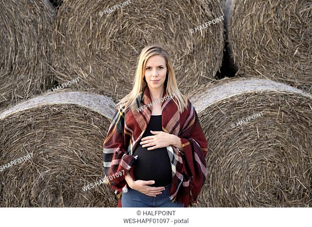 Smiling pregnant woman standing in front of bales of straw