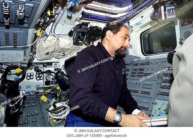 Astronaut Umberto Guidoni, mission specialist representing the European Space Agency (ESA), totes some notebooks of STS-100 mission data on the flight deck of...