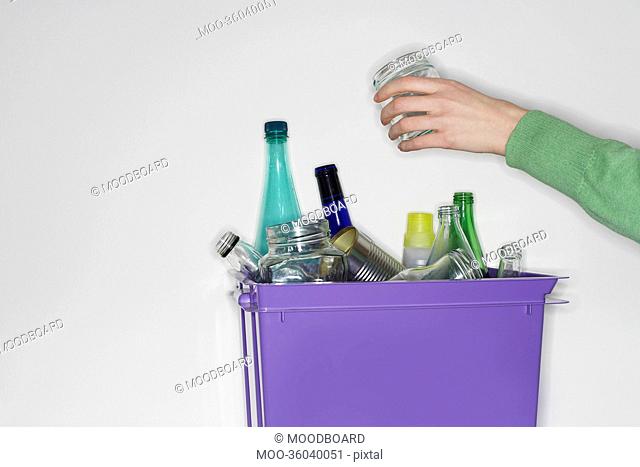 Person putting jar into recycling container filled with empty glass vessels