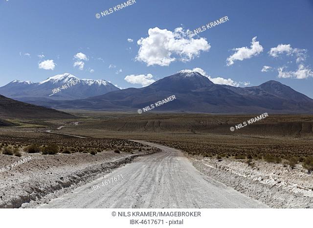 Gravel road leads through Altiplano, behind snow covered volcanoes, near Colchane, Tarapaca, Chile