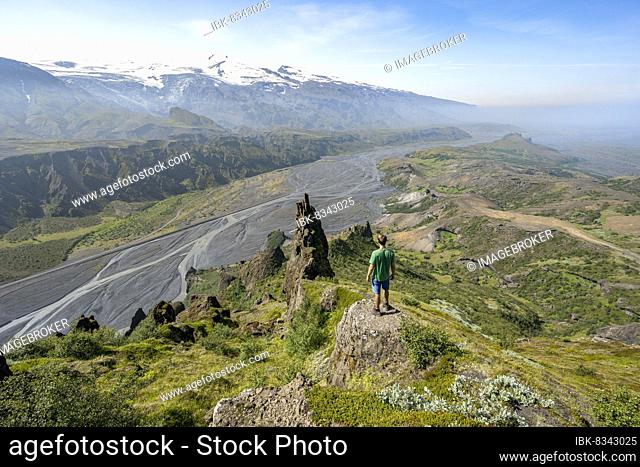 Hiker looking into the distance, rock formations at Valahnúkur peak, glacier river Krossá in a mountain valley, Eyjafjallajökull glacier in the back