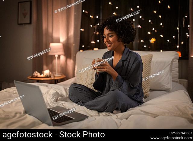 woman with laptop and mug sitting in bed at night
