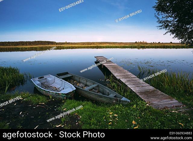 Wooden boards pier on Calm Water Of Lake, River and two rowing fishing boats