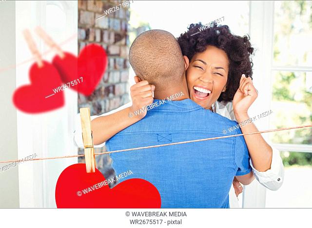 Composite image of red hanging hearts and excited couple embracing
