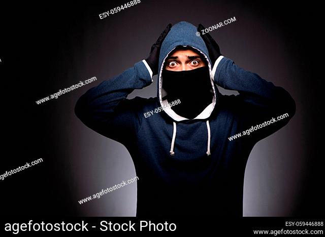 Young gangster in hood on grey background