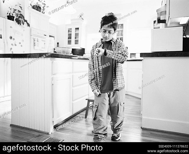 Young boy looking at watch in kitchen