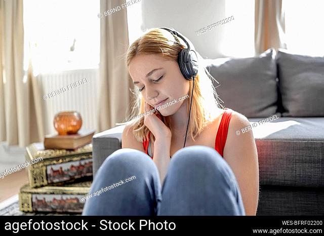 Portrait of young woman with eyes closed sitting on the floor at home listening music with headphones