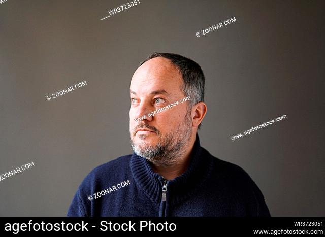 50 year old man with graying hair and beard looking away thinking - grey wall background with copy space