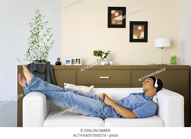 Young man relaxing on sofa listening to music with headphones