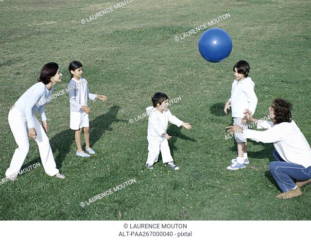 Parents with boys and girl playing ball on grass, full length