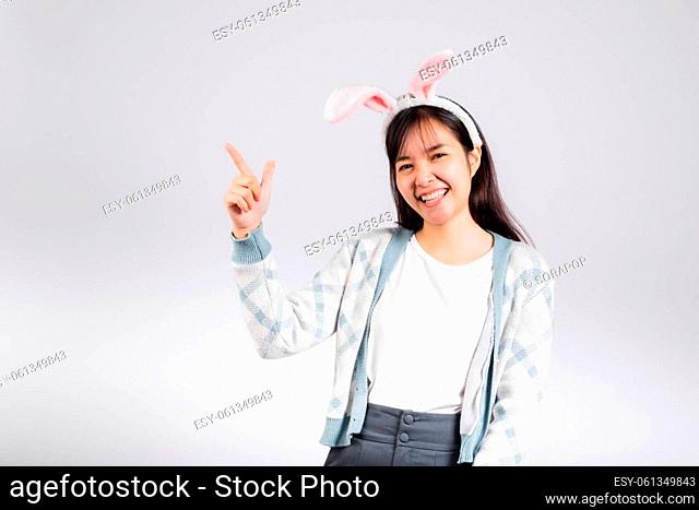 Easter day concept. Smiling happy woman wearing rabbit ears pointing finger something out space away side, studio shot isolated on white background with copy...