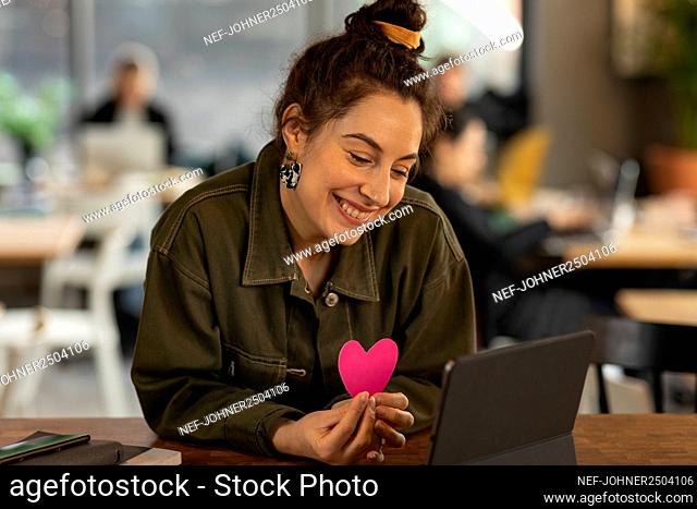 Smiling woman in cafe holding paper heart