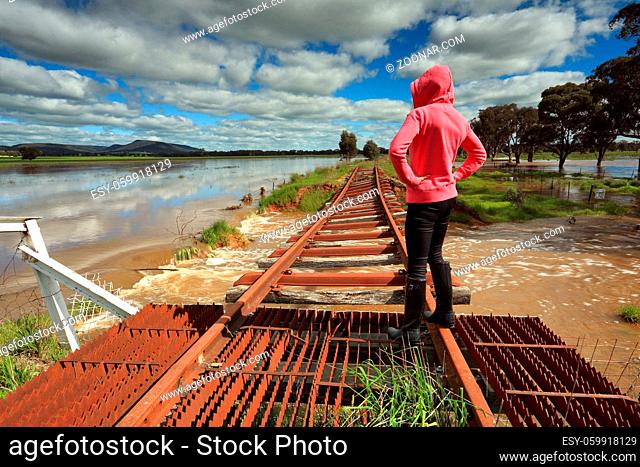 A female looks out over the floodwaters from the buckled train tracks at Crowther, Hilltops Region, Country NSW