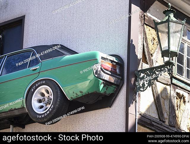 08 September 2020, Hessen, Brensbach: The left side of an old Ford Granada, cut lengthwise, is mounted on two supports on the facade of a house