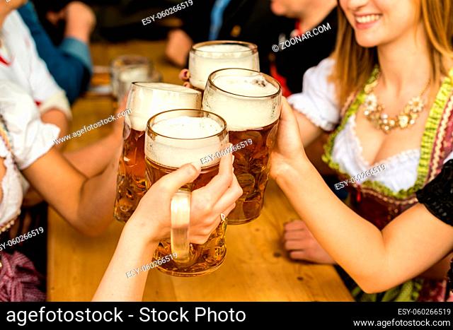 Bavarian girls in traditional Dirndl dresses are drinking beer and having fun at the Oktoberfest