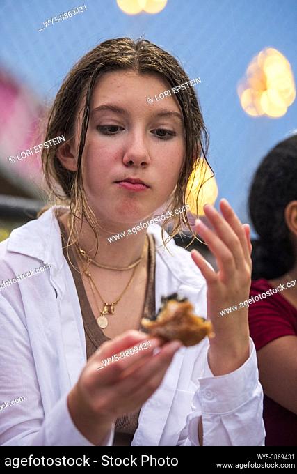 A caucasian teenage girl eats a deep-fried Oreo cookie at the county fair in Arlington, Virginia