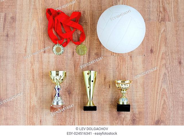 sport, achievement, championship, competition and success concept - close up of volleyball ball with golden medal and cup over wooden background