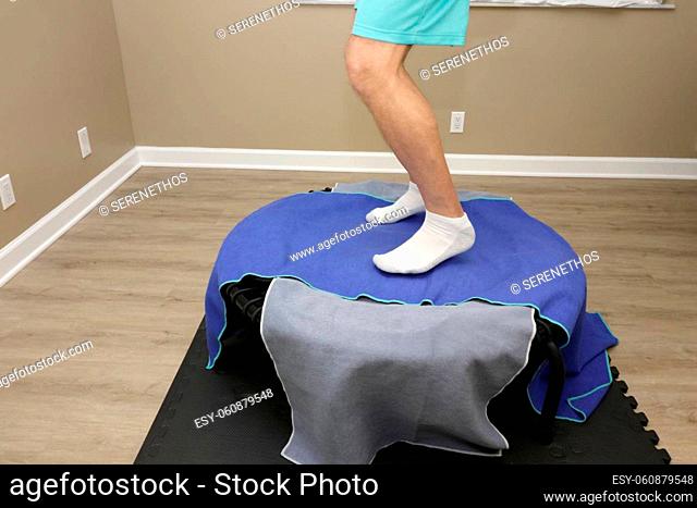 Adult white male feet and legs jumping on a round black mini trampoline also called a rebounder. Rebounder with two workout towels being jumped on by adult...