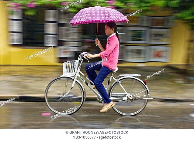 Vietnamese girl cycling in the rain, Hoi An, Vietnam