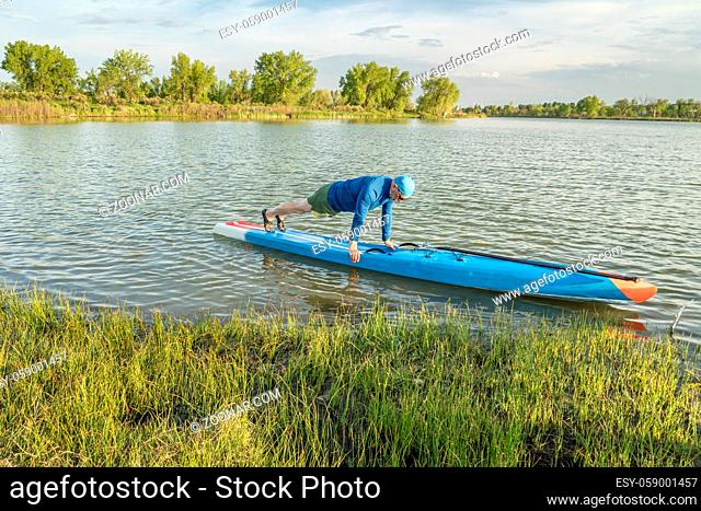senior paddler is warming up by doing pushups before workout on a stand up paddleboard